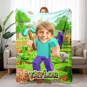 May include: A Minecraft-themed blanket featuring a boy's face superimposed on a pixelated character holding a pickaxe. The blanket has a green and blue landscape background with Minecraft characters and the name "Taylor".