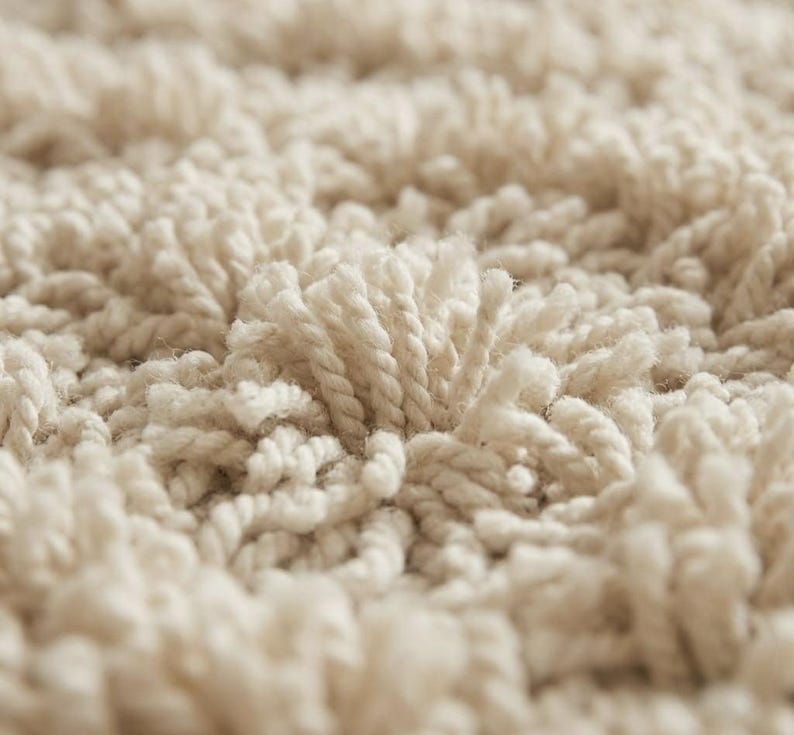 May include: A high-pile rug featuring a dense, textured surface made of off-white, twisted yarn loops. The material creates a thick, shaggy appearance with a consistent, monochromatic cream color throughout the entire visible area.