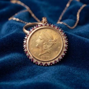 Op de afbeelding: Een gouden munthanger met een profielportret van Lady Liberty en het jaartal 1879. De munt is omlijst door een cirkelvormige rand van afwisselend kleine heldere witte stenen en donkerrode stenen aan een gouden ketting.