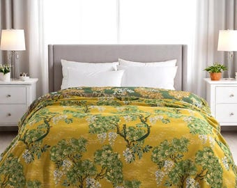 Puede incluir: Una manta amarilla y verde con un diseño botánico con árboles y flores. La manta tiene un borde con flecos y está colocada sobre una cama. La paleta de colores incluye tonos de amarillo, verde y blanco.