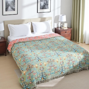 May include: A bed with white pillows and a green floral patterned blanket. The blanket has a fringe along the bottom edge and a coral-coloured border. The room has a neutral colour palette with framed artwork.
