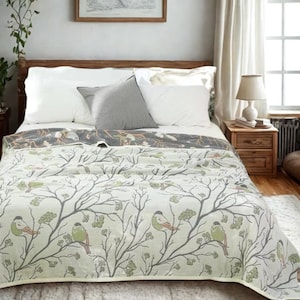 Può includere: Un letto è fatto con cuscini bianchi e un cuscino grigio. Una coperta fantasia con un disegno di uccelli e rami copre il letto. La coperta ha uno sfondo bianco con rami grigi e uccelli verdi.