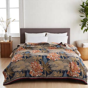 Può includere: Una coperta da letto blu navy e beige a fantasia con un design botanico con palme e altro fogliame. La coperta è drappeggiata su un letto con cuscini bianchi e una testiera grigia. I bordi hanno una striscia rossa e bianca.