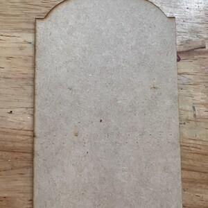 May include: A rectangular wooden plaque with an arched top. The plaque is made of light brown wood and has a smooth surface. It is likely intended for crafting or personalization.