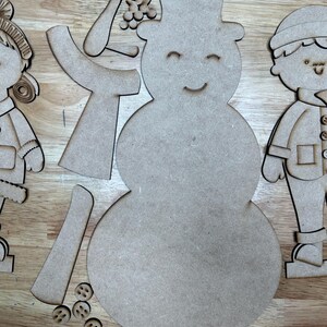 以下が含まれることがあります： クラフト用の、未完成の木製雪だるまと子供たちの切り抜き。雪だるまはシルクハット、笑顔の顔、別々の腕、ベリーの枝を持っています。子供たちは冬服を着ています。小さな木製のボタンが含まれています。