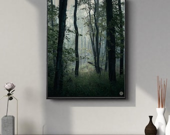 May include: A framed print of a forest scene with tall trees and green foliage. The artwork is in a black frame and hangs on a white wall. A dark wooden surface in the foreground holds decorative vases and a flower.
