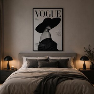 May include: A framed wall art print featuring a black and white photograph of a person wearing a wide-brimmed hat, with the text VOGUE at the top. The print is displayed above a bed with grey bedding, two dark nightstands, and two black lamps.