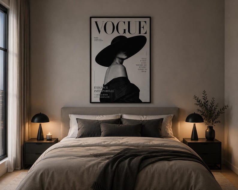 May include: A framed wall art print featuring a black and white photograph of a person wearing a wide-brimmed hat, with the text VOGUE at the top. The print is displayed above a bed with grey bedding, two dark nightstands, and two black lamps.