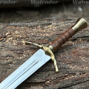 Pode incluir: Uma espada com lâmina de aço polido em tom prateado, guarda de latão com design torcido e cabo revestido em couro castanho com pomo de latão. A lâmina possui um sulco central que percorre o seu comprimento a partir da guarda.