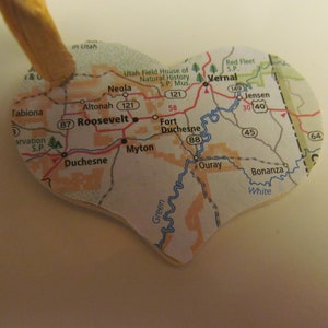 Puede incluir: Adorno en forma de corazón con un mapa de Utah, con ciudades como Roosevelt y Vernal. Tiene una cinta beige adjunta. El mapa detalla carreteras y ríos. Un artículo decorativo único.