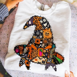 May include: White sweatshirt featuring a colorful, patchwork-style witch hat design. The hat incorporates various Halloween-themed patterns and images, including pumpkins, ghosts, and stars. The design is stitched onto the front of the sweatshirt.