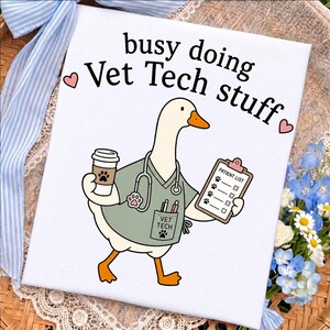May include: A white rectangular sign featuring a cartoon goose wearing a sage green scrub top with a stethoscope, holding a coffee cup and a patient list clipboard. The text reads busy doing Vet Tech stuff with two small pink hearts.