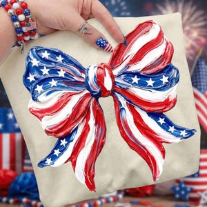 May include: A cream-colored pillow with a large, textured bow design in red, white, and blue, resembling the American flag. The bow features white stars on a blue background and red and white stripes. The pillow is a patriotic decorative item.