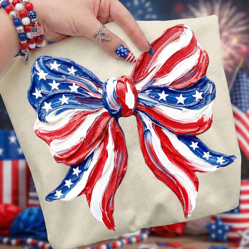 May include: A cream-colored pillow with a large, textured bow design in red, white, and blue, resembling the American flag. The bow features white stars on a blue background and red and white stripes. The pillow is a patriotic decorative item.