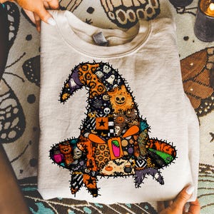 May include: A beige crewneck sweatshirt featuring a large, central graphic of a witch hat constructed from a patchwork of various Halloween-themed patterns, including pumpkins, ghosts, spiderwebs, bats, and orange leopard print with black stitching.