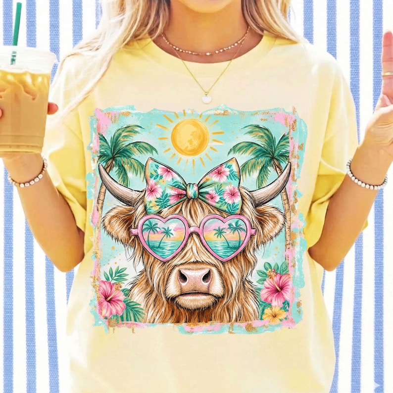 May include: A pale yellow t-shirt featuring a graphic of a highland cow wearing heart-shaped sunglasses with a tropical beach reflection. The cow has a floral bow between its horns, set against a background of palm trees and a yellow sun.