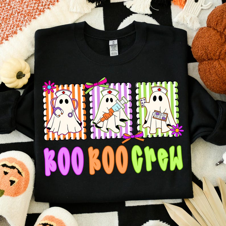May include: Black sweatshirt with a colorful graphic featuring three ghost characters dressed as nurses, each with medical tools. The text "BOO BOO CREW" is below the graphic in pink, orange, and green. A fun Halloween design.