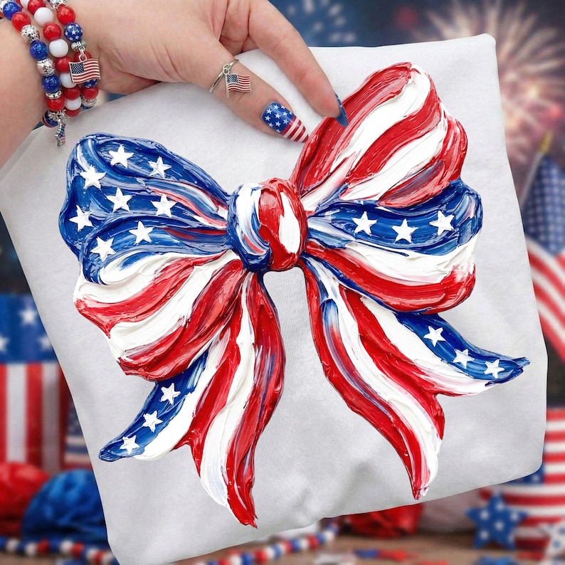 May include: A white pillow with a large, textured bow design in red, white, and blue, reminiscent of the American flag. The bow features white stars on a blue background and red and white stripes.