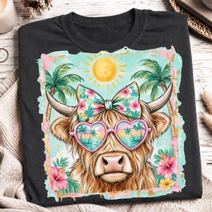 May include: A black t-shirt featuring a graphic of a Highland cow wearing heart-shaped sunglasses with a tropical beach reflection. The cow has a floral bow on its head, surrounded by palm trees, a yellow sun, and pink hibiscus flowers.