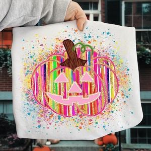 May include: White tote bag featuring a colorful, striped pumpkin design with a smiling face. The pumpkin has a brown stem and is surrounded by colorful paint splatters. A fun and festive Halloween-themed accessory.
