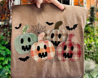 May include: A brown fabric item featuring four appliqued pumpkins in various patterns and colors, including green, orange, and red plaid. Black bats and spiderwebs decorate the background, creating a Halloween theme.