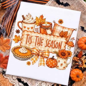 May include: A white rectangular canvas featuring a colorful autumn-themed illustration with the text 'TIS THE SEASON'. The design includes a mug with whipped cream, a candle, a pumpkin pie, a plaid pillow, a bow, a pumpkin, and a floral pitcher.