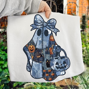 Op de afbeelding: Een witte Halloween-tas met een patchwork spookontwerp. Het spook heeft een spijkerstrik en draagt een pompoenvormige mand. Het ontwerp bevat pompoen- en katmotieven.