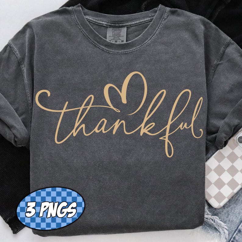 May include: Dark gray long-sleeve shirt with the word "thankful" in a cursive font and a heart above the word. The shirt has a vintage, washed look. A small graphic that says "3 PNGS" is in the lower left corner.