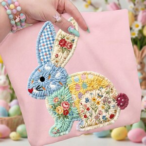 May include: A pink fabric item with a patchwork bunny design. The bunny has blue gingham ears, a blue body with white rabbits and carrots, and a floral and butterfly-filled body. The bunny's tail is a small, round, red and white polka-dotted design.