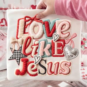 May include: White fabric with the phrase "LOVE LIKE JESUS" in a colorful, textured design. The letters are in red, pink, and blue, with decorative hearts, bows, and a disco ball heart. A black and white star is also included.