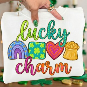May include: White sweatshirt with a colorful "Lucky Charm" design. The design includes a rainbow, a shamrock square, a heart, and a pot of gold. The text is in green, blue, pink, and orange.