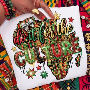 Op de afbeelding: Wit t-shirt met een kleurrijke kaart van Afrika en de tekst "do it for the CULTURE" in glinsterend groen, rood en zwart. Het ontwerp bevat sterren en een strik. Het t-shirt toont Afrikaans geïnspireerde patronen.