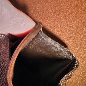 May include: Close-up of a brown leather wallet interior. The interior is black with a brown trim. The wallet has a textured pattern on the exterior. The word "DOLL" is visible on the interior.