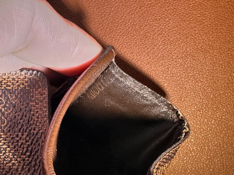 May include: Close-up of a brown leather wallet interior. The interior is black with a brown trim. The wallet has a textured pattern on the exterior. The word "DOLL" is visible on the interior.