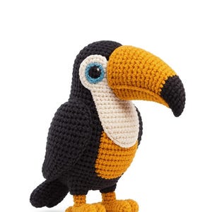 Puede incluir: Un tucán de ganchillo hecho a mano con un gran pico amarillo y negro. El ave tiene plumas negras, pecho color crema y patas amarillas. Los ojos son azules con un contorno blanco.