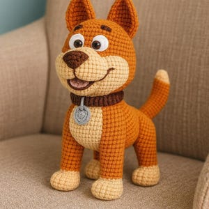 Puede incluir: Un juguete de perro de ganchillo hecho a mano en tonos naranja y beige. El perro tiene ojos grandes y expresivos, una nariz marrón y un collar con una etiqueta. El juguete está sobre una superficie de color neutro.