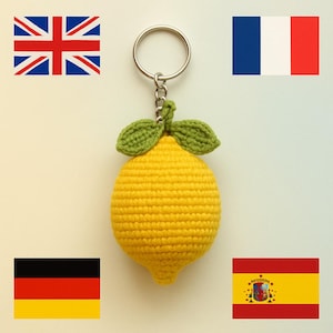Pode incluir: Um chaveiro de limão amarelo feito à mão com folhas verdes. O chaveiro tem um anel e uma corrente prateados. A imagem também inclui as bandeiras do Reino Unido, França, Alemanha e Espanha.