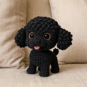 May include: A handmade black crochet dog with large, expressive eyes and a pink tongue. The plush toy has a curly texture and is posed on a neutral-toned sofa. This adorable dog is a charming addition to any collection.