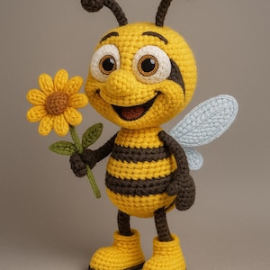 Op de afbeelding: Gehaakte bijenpop met een geel en bruin gestreept lichaam, met een gele bloem. De bij heeft grote, vriendelijke ogen, bruine antennes en lichtblauwe vleugels. Hij draagt gele laarzen en heeft een glimlachende uitdrukking.