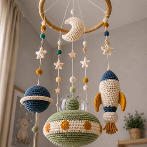 Könnte beinhalten: Handgefertigtes Baby-Mobile mit Holzring und gehäkelten Elementen: Planeten, Sterne, Mond und Rakete. Die Planeten sind blau und grün, die Sterne aus Holz, die Rakete mit gelben Details.