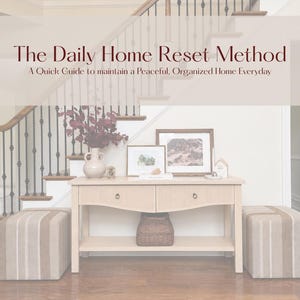 Peut inclure: Un guide numérique intitulé The Daily Home Reset Method: A Quick Guide to maintain a Peaceful, Organized Home Everyday. Le texte est superposé sur une console en bois clair avec deux tiroirs, une étagère inférieure et deux poufs rayés.