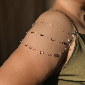 May include: Delicate shoulder jewelry featuring three strands of clear, thin chain adorned with clear and amber-colored beads. The jewelry is clipped to the shoulder and arm, creating a unique and elegant accessory.