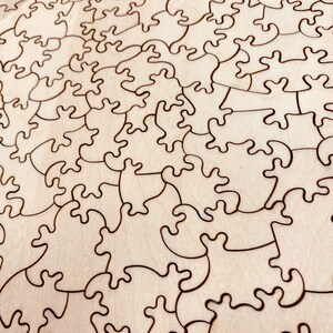 May include: A close-up of a wooden jigsaw puzzle with a natural wood finish. The puzzle pieces are cut in a unique, intricate design, creating a complex and challenging puzzle.