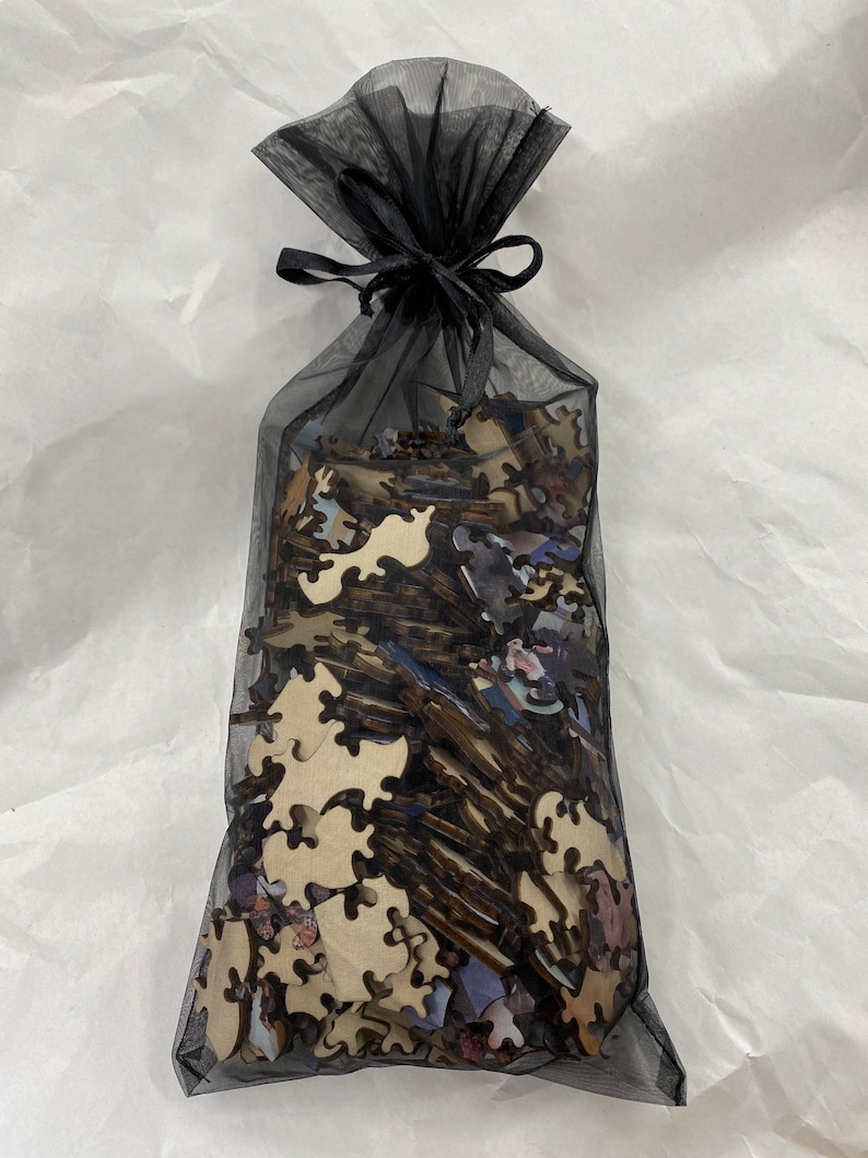 May include: A black mesh bag filled with a wooden jigsaw puzzle. The pieces are scattered inside the bag.