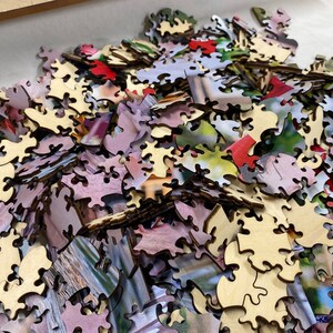 May include: A pile of wooden jigsaw puzzle pieces with a variety of colors and images. The pieces are scattered on a white surface.