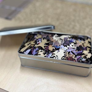 A metal container filled with puzzle pieces is placed on a wooden surface.