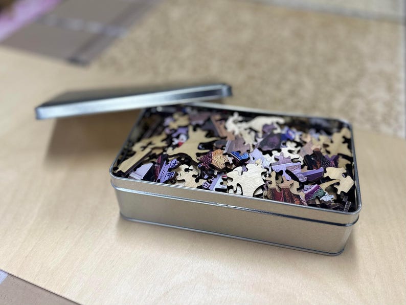 A metal container filled with puzzle pieces is placed on a wooden surface.