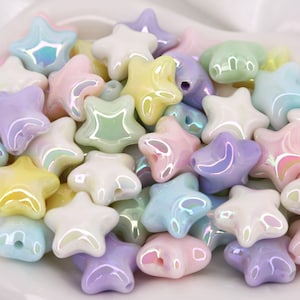May include: A collection of pastel-colored star-shaped beads. The beads are in shades of pink, yellow, blue, green, and purple, with an iridescent sheen. Each bead has a hole for stringing. The beads are likely for jewelry making or crafts.