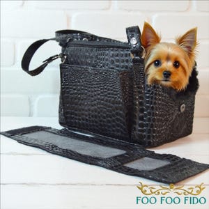 May include: Black faux-leather pet carrier with a textured, crocodile-like pattern. A small, tan and brown Yorkshire Terrier dog is peeking out of the carrier. The carrier has a handle and a detachable, zippered section. The text "FOO FOO FIDO" is at the bottom.