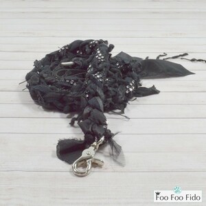 May include: Black dog leash with a silver clasp. The leash is made of braided fabric with a sparkly, beaded trim.